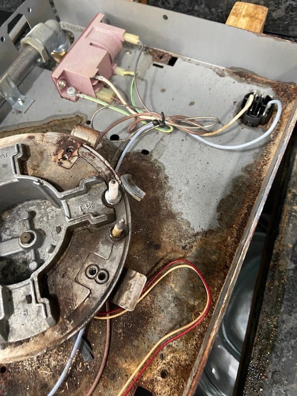 The stripped internals of a gas hob during repair, wiring and burner base exposed